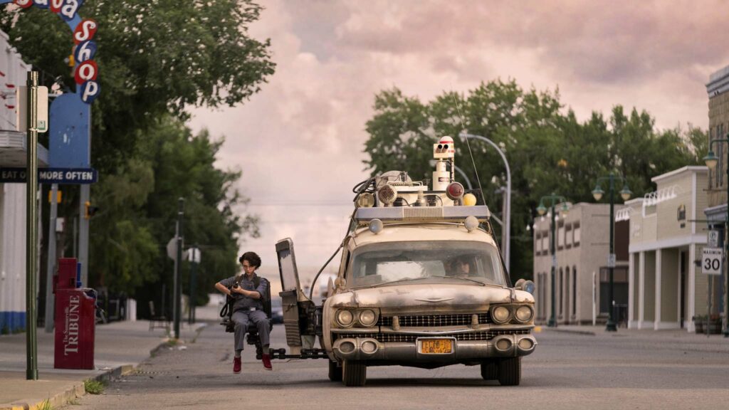 Mckenna Grace as Phoebe in the Ecto-1 jump seat with Finn Wolfhard as Trevor at the wheel in Ghostbusters: Afterlife, directed by Jason Reitman. Photo: Kimberley French. Copyright: 2019 CTMG, Inc. All Rights Reserved.