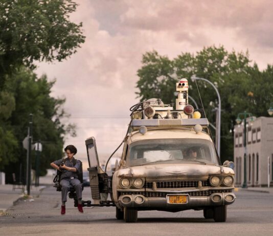 Mckenna Grace as Phoebe in the Ecto-1 jump seat with Finn Wolfhard as Trevor at the wheel in Ghostbusters: Afterlife, directed by Jason Reitman. Photo: Kimberley French. Copyright: 2019 CTMG, Inc. All Rights Reserved.