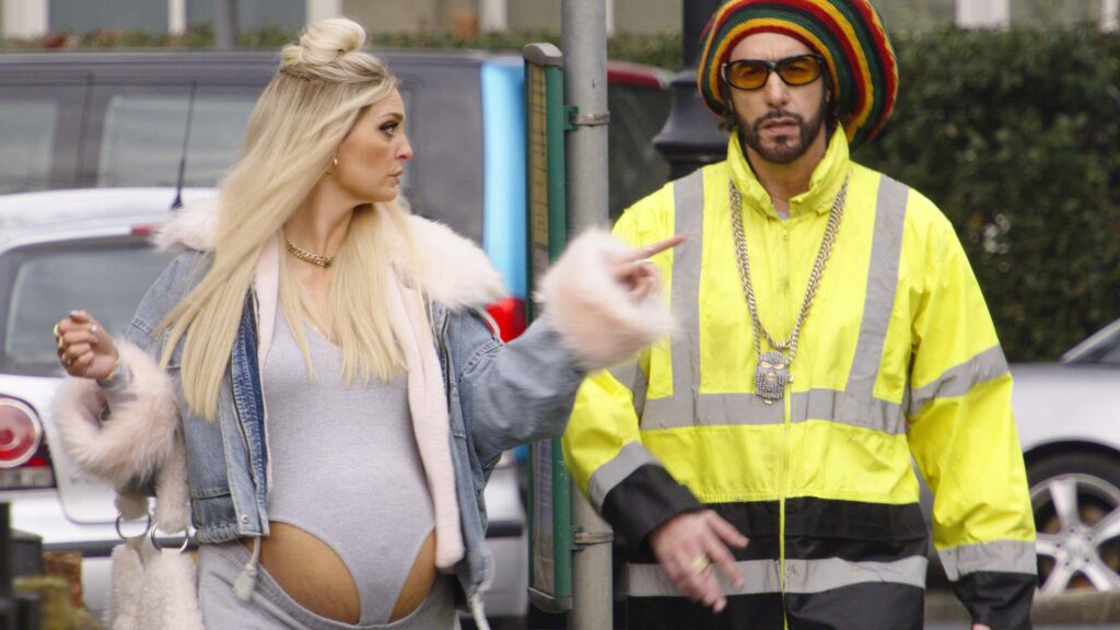 Morgana Robinson as Julie and Sacha Baron Cohen as Ali G in Ali G: Who Iz I?, directed by Sacha Baron Cohen. Copyright: Amazon Content Services LLC. All Rights Reserved.